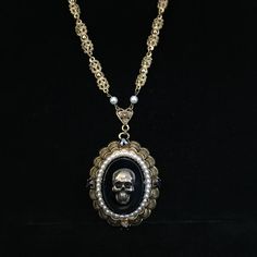 This is a large, circa 1930s, antiqued brass necklace with added brass skull. The large 2 x 1.75 inch pendant has great Victorian elements. The skull on the 1.25 x 1 inch, hematite-colored smooth glass center measures .75 inch and has been added to this vintage necklace. Even the dog tooth prongs holding the center stone in are detailed. It is surrounded by several tiny faux pearls. On the detailed, gold plated scalloped framework are four, .25 inch cut hematite-colored glass stones.  The hemati Gothic Metal Skull Necklace, Nickel-free Antique Gold Metal Jewelry, Antique Finish Brass Medallion Jewelry, Steampunk Skull Jewelry Gift, Vintage Halloween Pendant Jewelry, Gold Metal Necklace For Halloween, Antique Gold Metal Jewelry With Antique Finish, Gothic Pendant Necklace With Antique Finish, Vintage Brass Long Necklace With Charm