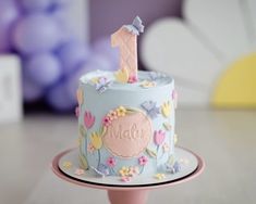 a blue cake decorated with flowers and a pink number one on it's top