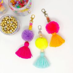 three tasseled keychains with beads and other items on a white surface