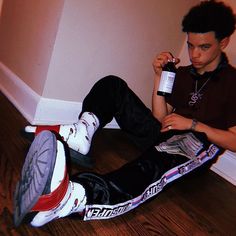 a young man sitting on the floor with his feet up and holding a bottle of water