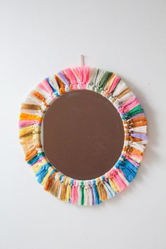 a mirror that is made out of different colored yarns and has a brown frame