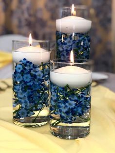 three glass vases filled with blue flowers and lit candles sitting on top of a table