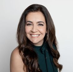 a smiling woman with long dark hair wearing a green top and black scarf around her neck