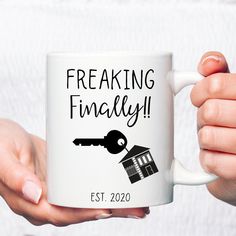 two hands holding a coffee mug with a house and key on it that says freaking finally