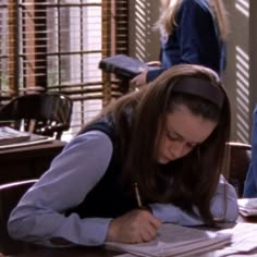 a woman sitting at a desk writing on a piece of paper with a pencil in her hand