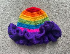 a crocheted hat with ruffles on the bottom sits on a carpet