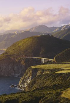 a scenic view of the ocean and mountains with a bridge going over it in the foreground