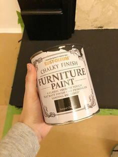 a person holding a can of furniture paint in front of a black and white wall