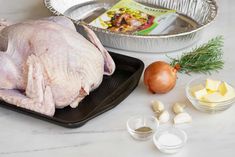 raw chicken and ingredients laid out on a counter top, including onions, garlic, butter, seasoning powder, and an aluminum pan