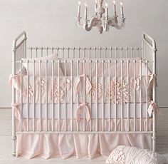 a baby crib with pink ruffled bedding and chandelier