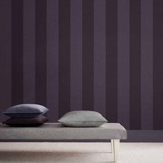 a bed with two pillows on top of it in front of a purple striped wall