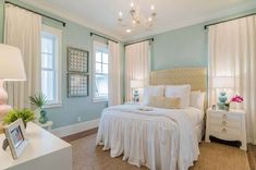 a bedroom with light blue walls and white bedding, two windows, and a chandelier hanging from the ceiling