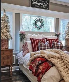 a bedroom decorated for christmas with plaid pillows and blankets on the bed, wreaths hanging above