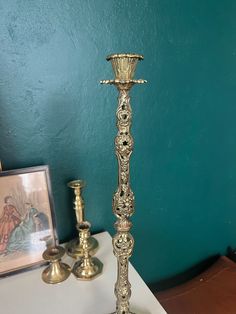 a tall metal candle holder sitting on top of a white table next to a painting