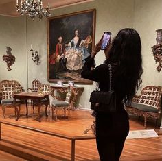 a woman taking a photo of a painting in a room with wooden floors and chairs