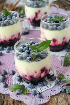 three desserts with blueberries and cream in small glasses on a purple doily