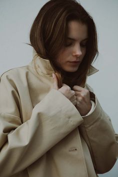 a woman in a trench coat is holding her hand on her shoulder and looking down