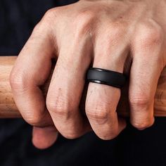 a man's hand with a black ring on his finger holding a baseball bat