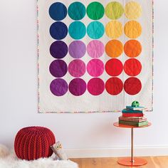 a colorful quilt hanging on the wall next to a small table with a stuffed animal