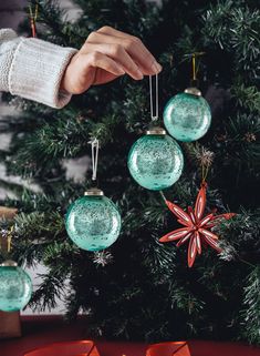 a person placing ornaments on top of a christmas tree ornament hanging from strings