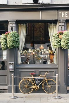 a bicycle is parked in front of a storefront with flowers hanging from the windows