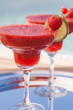 two glasses filled with watermelon margaritas on top of a blue table next to the ocean