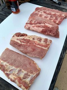 three pieces of meat sitting on top of a white cutting board