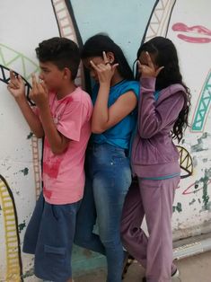 three children leaning against a wall with their hands together