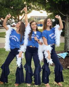 three girls in blue shirts and white feather boas posing for the camera with their arms up