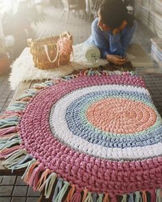 a woman sitting on the floor next to a rug with yarn and crochet