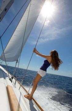 a woman standing on the deck of a sailboat in the open ocean with sun shining down