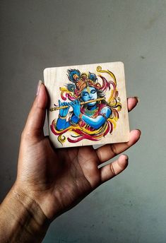 a hand holding a small wooden box with an image of a god on it