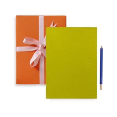 an orange and yellow notebook with a bow on the cover next to a blue pen