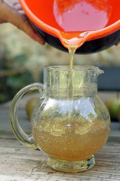 a pitcher filled with liquid sitting on top of a wooden table next to an orange bowl