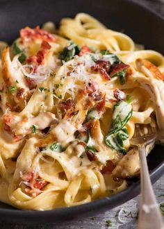 pasta with chicken, spinach and cheese in a black bowl next to a fork