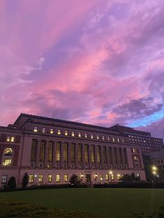 the building is lit up at night in front of some pink and blue sky with clouds