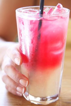 a person holding a drink with a straw in it's hand on a wooden table