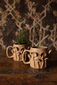 two clay mugs sitting on top of a wooden table next to a planter