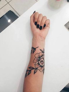 a woman's arm with black and white flowers on it, sitting at a table