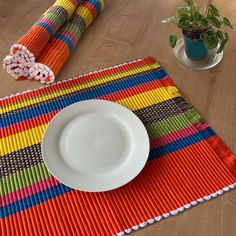 a white plate sitting on top of a colorful place mat next to a potted plant