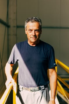 an older man standing in front of a yellow rail with his hands on his hips