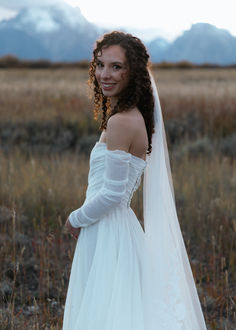 a woman in a wedding dress standing in a field with her arms around her waist