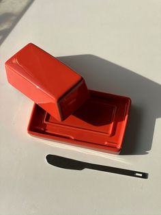 an orange container sitting on top of a white table next to a knife and fork