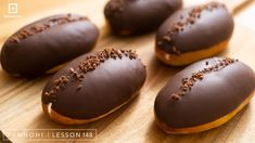 four chocolate covered donuts sitting on top of a wooden cutting board