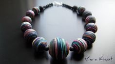 a necklace made out of multicolored paper beads on a black surface with the words vera kleit written below it