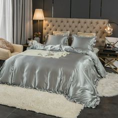 a bed with silver sheets and pillows in a room next to a couch, chair and lamp