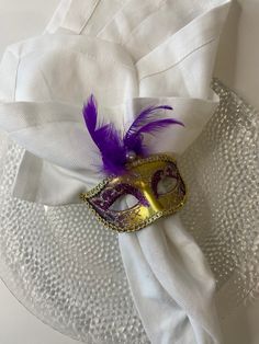 a masquerade on a white cloth with purple feathers and a gold eye mask