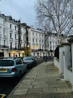 several cars parked on the side of a street next to tall white buildings and trees