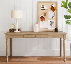 a wooden table with a clock, lamp and pictures on it in front of a white wall