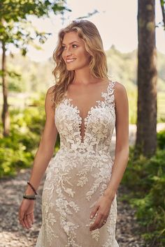 a woman in a wedding dress standing on a path with trees and bushes behind her